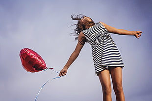 woman in white and black striped sleeveless dress holding red heart balloon in worms eye photography