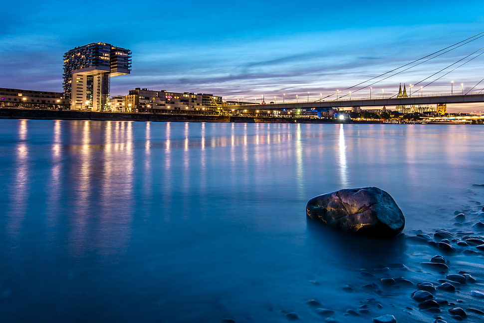 rock beside river near lighted buildings HD wallpaper