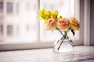 pink and yellow flowers in vase beside window