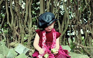 girl with black leather hat and pink dress holding fruit with trees in background