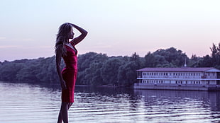 woman wearing red sleeveless dress standing beside body of water near white house