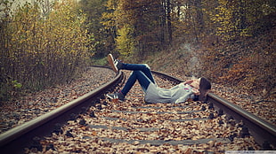 woman in blue jeans lying on train railway