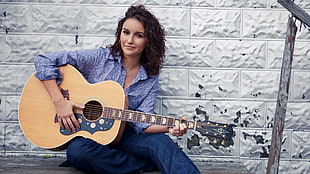 woman playing brown acoustic guitar