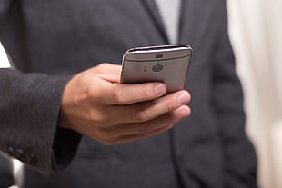 person holding grey HTC One M8 wearing black suit jacket