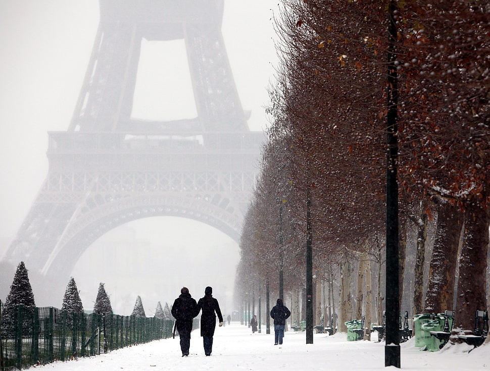 man and woman walking on snow coated road near the Eiffel Tower HD wallpaper