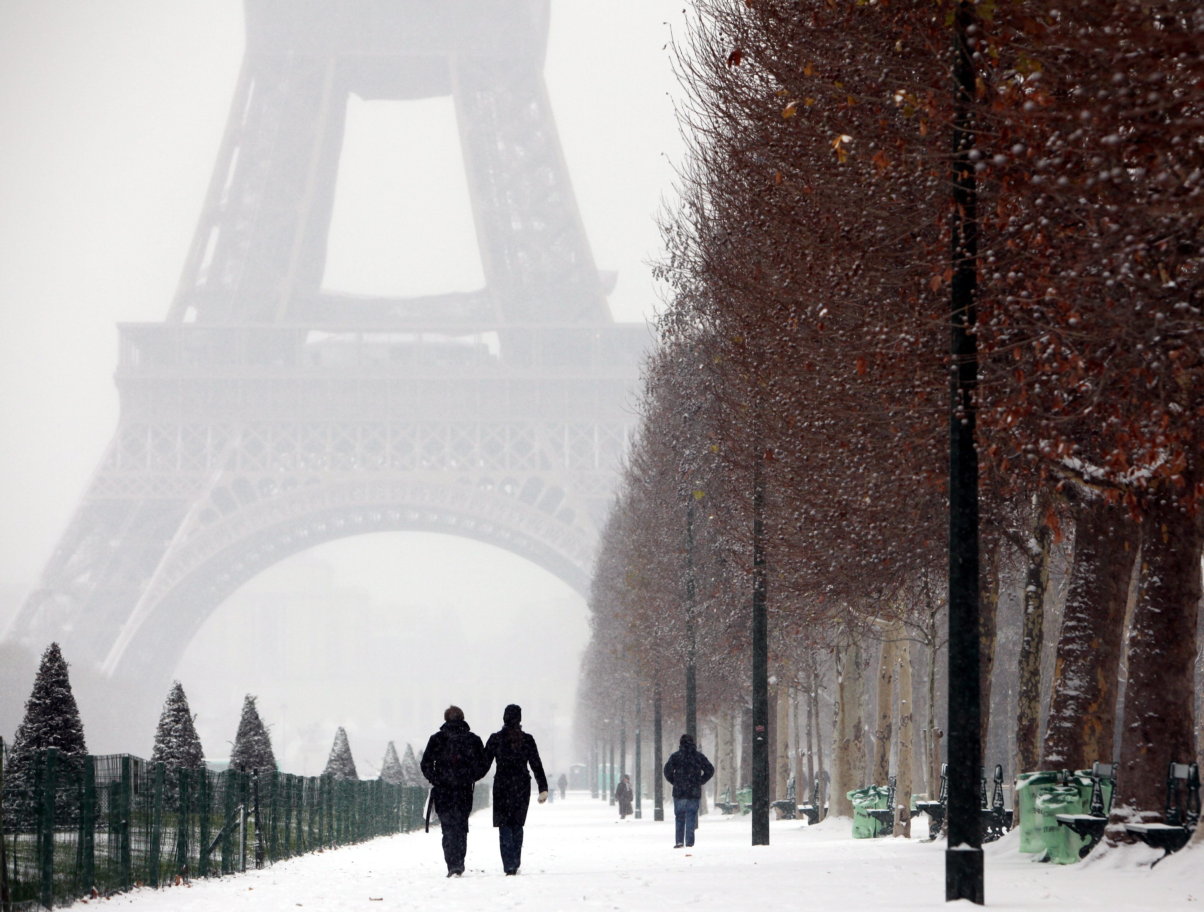 man and woman walking on snow coated road near the Eiffel Tower