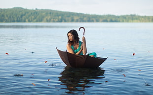 woman in green sleeveless dress rides on open umbrella over body of water during daytime