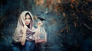 woman wearing brown hijab holding black bird and brown bird cage HD wallpaper