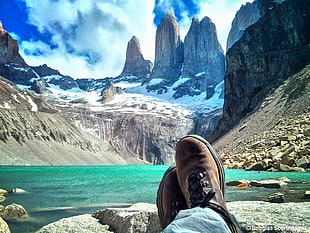 person in blue denim jeans and brown lace-up shoes in front of snow covered mountains during daytime