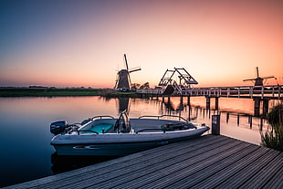 white and  teal motorboat beside brown wooden walk way bridge during sun set, kinderdijk, holland