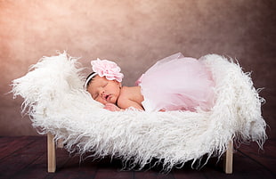baby in pink tutu skirt sleeping on white fur mat close-up photo