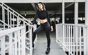woman in black long-sleeved crop top and black pants standing gray rails at daytime