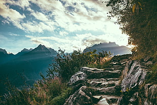 photo of gray rocky road on mountain side under blue and white sky