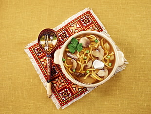 mushroom pasta soup dish on white ceramic bowl and spoon on top of red and white fringe table mat