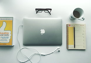 silver MacBook placed next to spring notebook and black framed eyeglasses