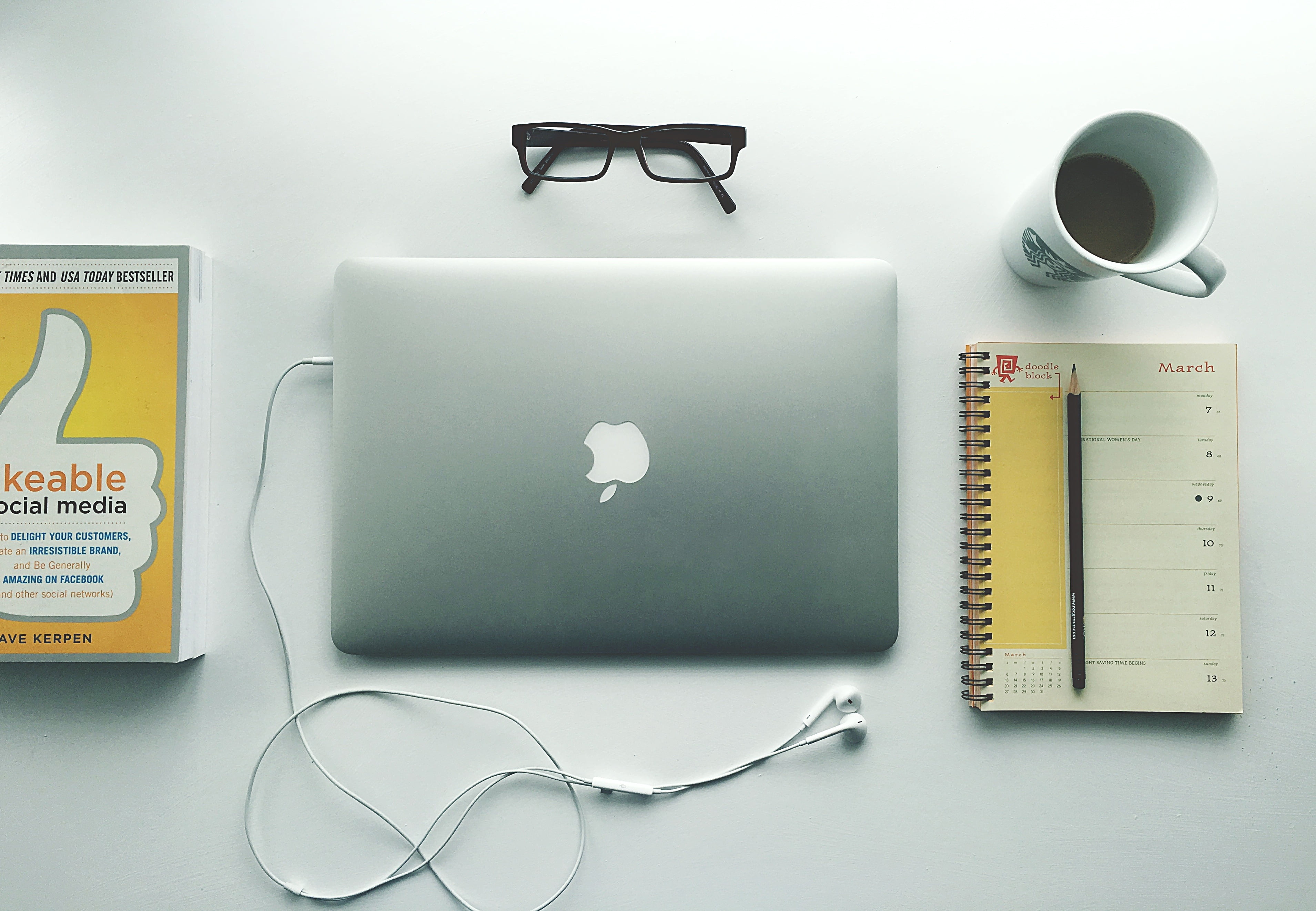 silver MacBook placed next to spring notebook and black framed eyeglasses