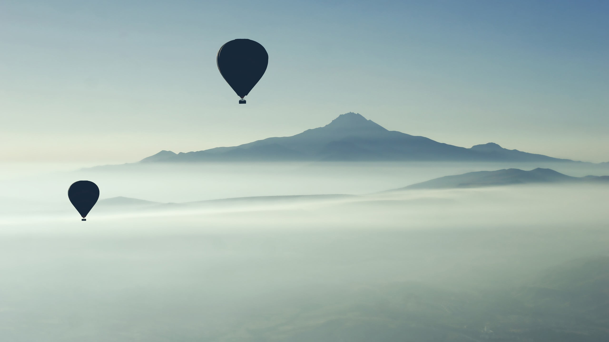 two silhouette of hot air balloons flying on sky with overlooking view coned mountain at daytime