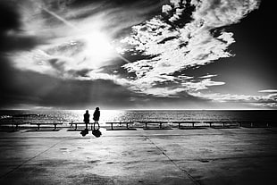 gray scale photo f man and woman in front of sea underneath clear sky during daytime
