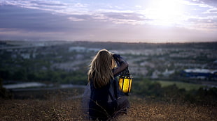 selective focus photography of a woman holding lantern lamp sitting in brown field