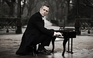 Dr. House actor wearing black top and black dress pants playing grand piano miniature on black surface