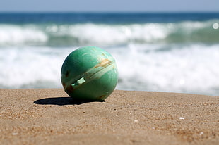 Shallow focus photography of Green plastic ball on sand near on body of water during daytime