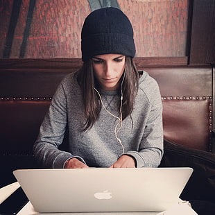 focus photo of woman facing her laptop wearing black knit cap and gray jacket with headset