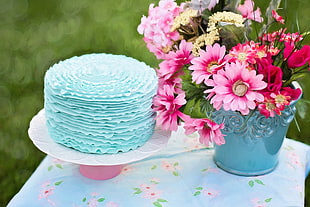pink and yellow flowers on blue ceramic vase beside blue cake
