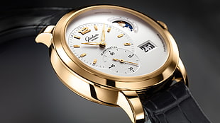 close up photo of round gold-colored chronograph watch with black strap