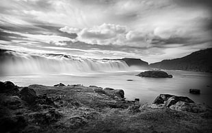 grayscale photo of water falls between cliff