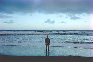man standing on sea shore during nighttime