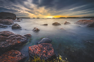 timelapse photo of body of water with rock formation during sunset