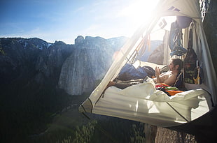 man lying on hanging tent near mountain cliff