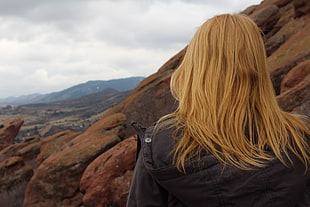 blonde haired woman wearing black jacket near mountain during daytime HD wallpaper