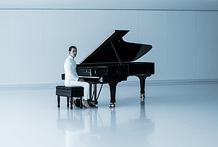 man in white dress shirt playing black grand piano with white background