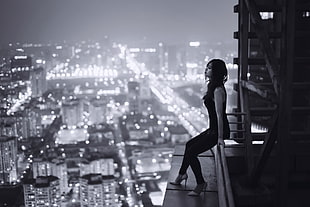 grayscale photo of woman sitting on building