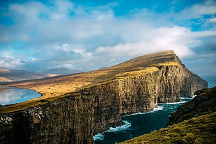 cliff surrounded by body of water under the cumulus clouds