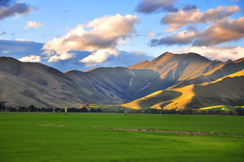 green grass field near mountain cloudy sky HD wallpaper