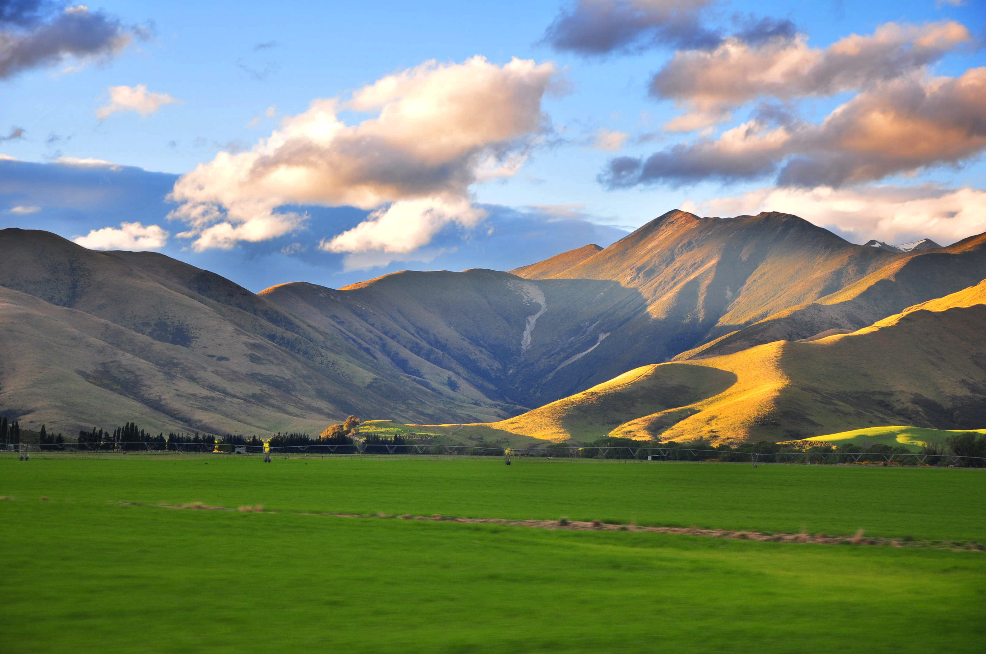 green grass field near mountain cloudy sky