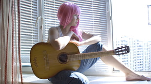 woman sitting holding guitar beside window