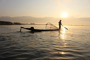 Silhouette of a fisherman on boat holding paddle in body of water during sunset