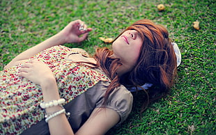 woman in gray and pink floral top lying on green lawn during daytime