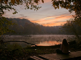 silhouette of woman sitting near lake during golden time HD wallpaper