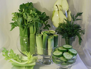 sliced green leaf vegetables and sliced cucumber on three clear glass bowls place on white table