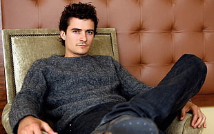 Orlando Bloom sitting on sofa chair wearing black sweater
