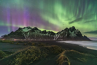 photograph of black mountain under green and purple aurora borealis