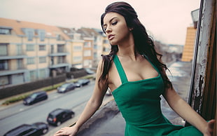 woman wearing green square-neck sleeveless dress sitting on the window during day