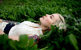 woman wearing white sleeveless shirt laying on green flower field