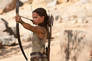 woman in gray tank top holding brown recurved bow and arrows
