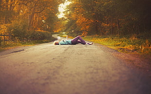 woman in teal shirt and purple pants lying in the road