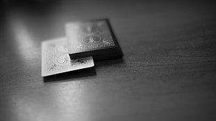 grayscale photo of two playing cards on brown wooden table